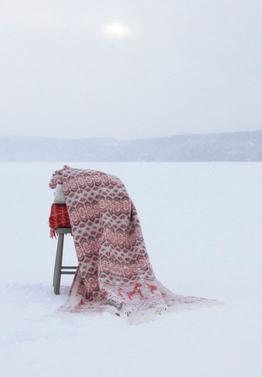 Röd ullfilt med dalahästar draperad på en stol i ett svenskt vinterlandskap